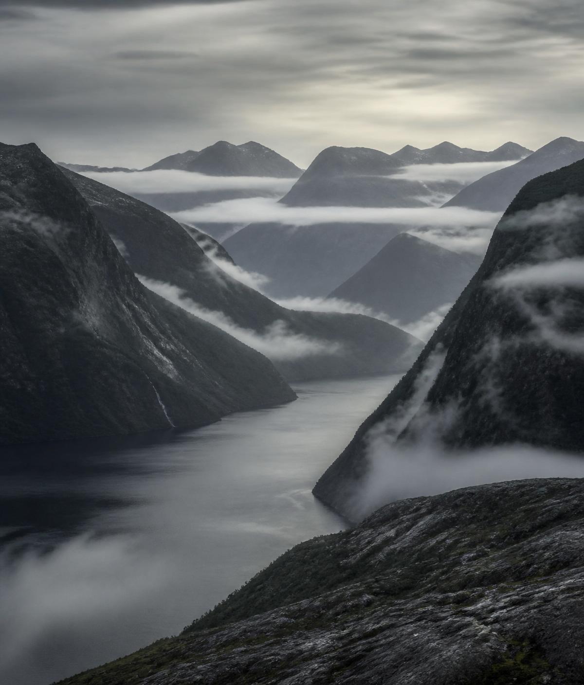 Nebelverhangene Berge über einem Fjord im Morgengrauen